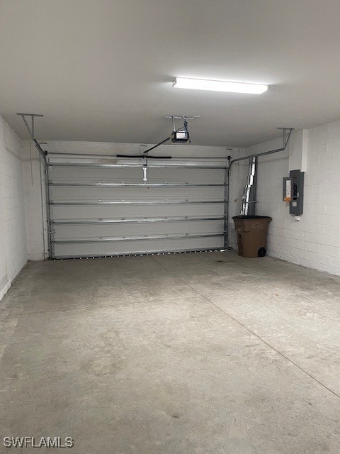 garage featuring electric panel, a garage door opener, and concrete block wall