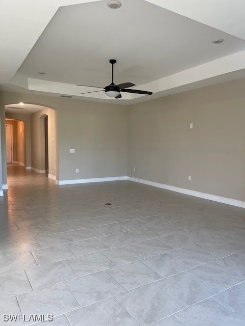 unfurnished room with a raised ceiling, a ceiling fan, arched walkways, and baseboards