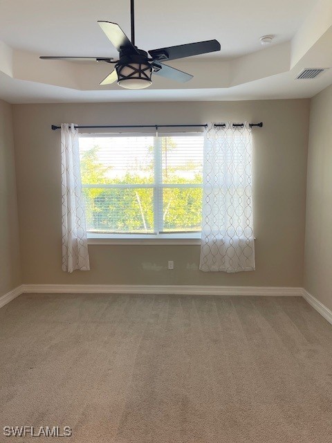 unfurnished room with a ceiling fan, baseboards, visible vents, a tray ceiling, and light carpet