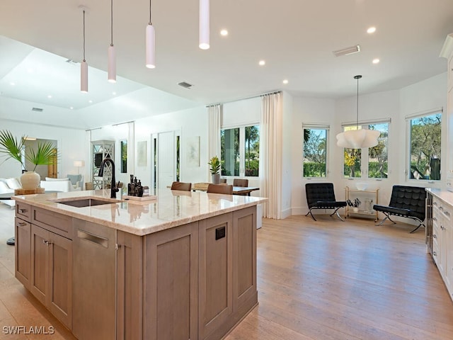 kitchen featuring light stone countertops, visible vents, a sink, open floor plan, and light wood-type flooring