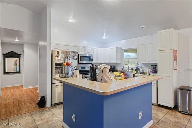 kitchen with lofted ceiling, white cabinets, an island with sink, and appliances with stainless steel finishes