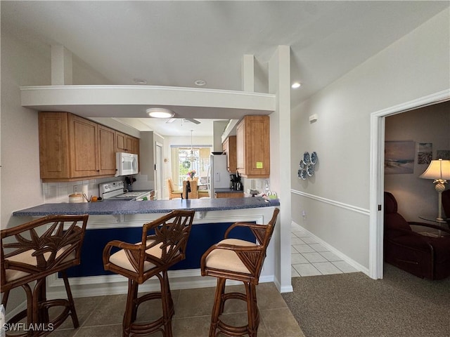 kitchen with tile patterned floors, dark countertops, tasteful backsplash, white appliances, and brown cabinetry