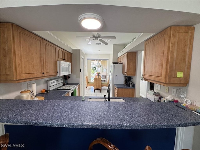 kitchen with a ceiling fan, a sink, dark countertops, white appliances, and a peninsula