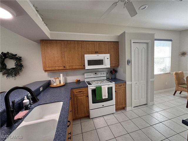 kitchen with light tile patterned floors, brown cabinetry, white appliances, a ceiling fan, and a sink