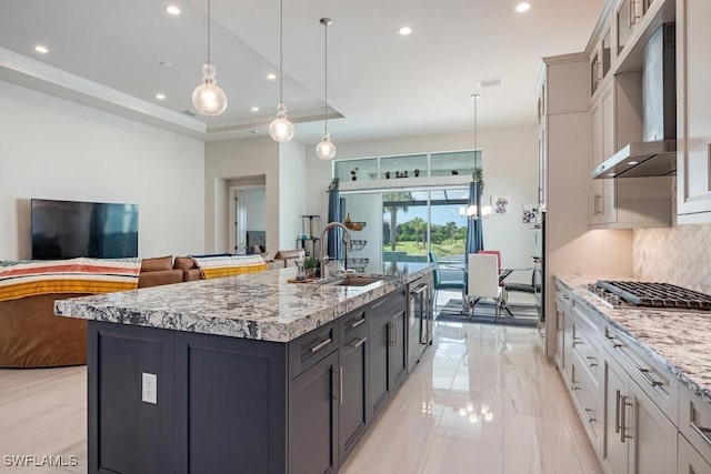 kitchen featuring wall chimney range hood, a tray ceiling, decorative backsplash, stainless steel gas stovetop, and a sink