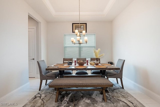 dining area with baseboards, a raised ceiling, and a chandelier