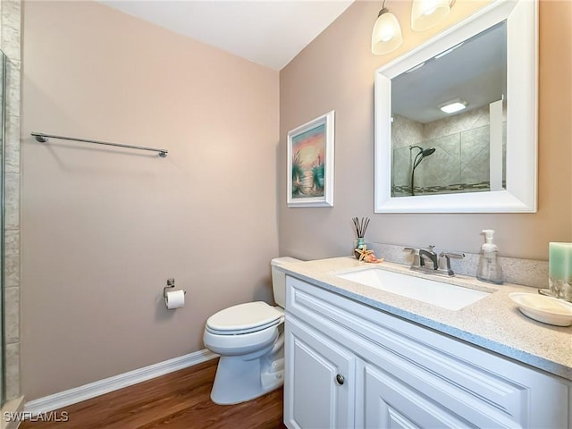 bathroom featuring baseboards, toilet, a tile shower, wood finished floors, and vanity