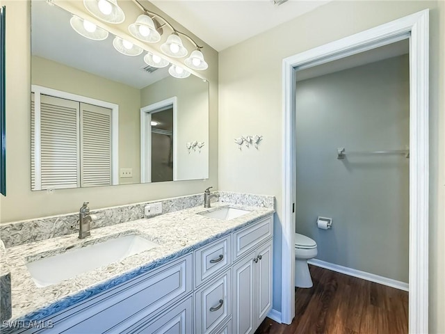 full bath with double vanity, toilet, wood finished floors, and a sink