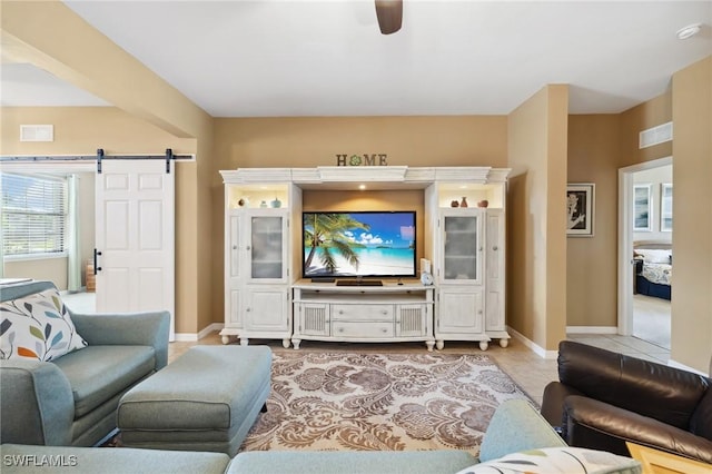 living area with light tile patterned floors, a barn door, baseboards, and ceiling fan