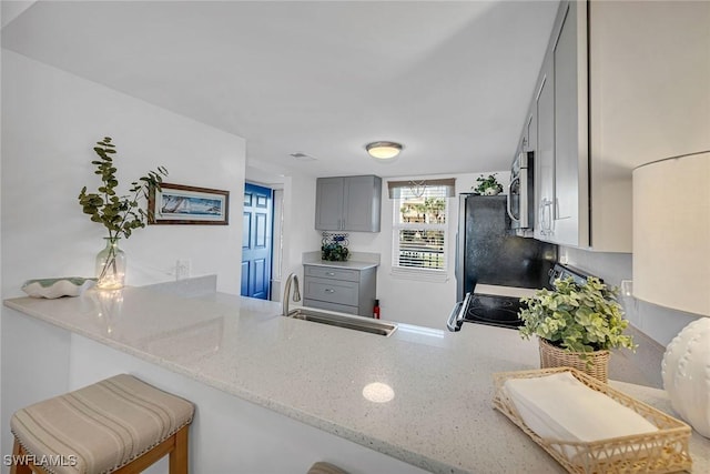 kitchen with stainless steel microwave, gray cabinetry, light stone countertops, a peninsula, and a sink