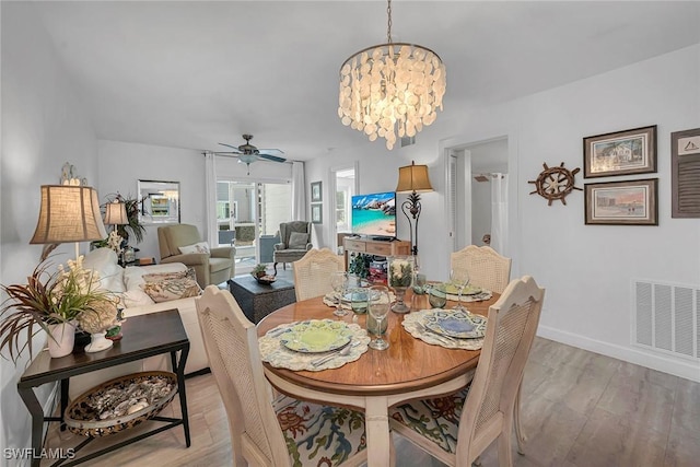 dining space with light wood-style floors, ceiling fan with notable chandelier, visible vents, and baseboards