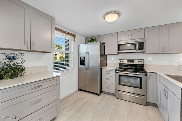 kitchen with gray cabinetry, baseboards, light countertops, light wood-style floors, and stainless steel appliances