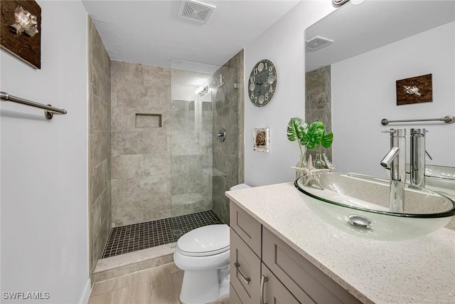 bathroom with vanity, toilet, visible vents, and tiled shower