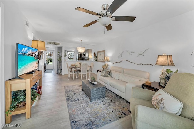 living area featuring light wood finished floors, visible vents, and ceiling fan with notable chandelier