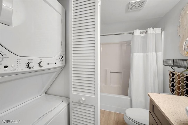 bathroom featuring visible vents, toilet, stacked washer and clothes dryer, wood finished floors, and shower / tub combo