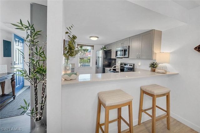 kitchen featuring a breakfast bar, light countertops, electric panel, gray cabinets, and appliances with stainless steel finishes