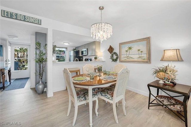 dining area with an inviting chandelier, light wood-style floors, and baseboards