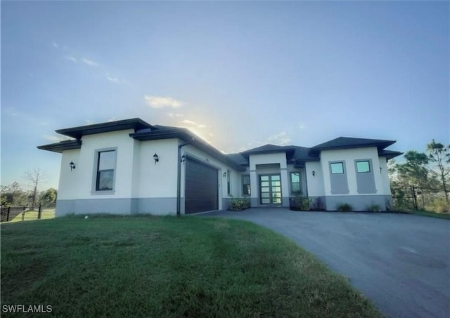 prairie-style home with fence, driveway, an attached garage, stucco siding, and a front lawn