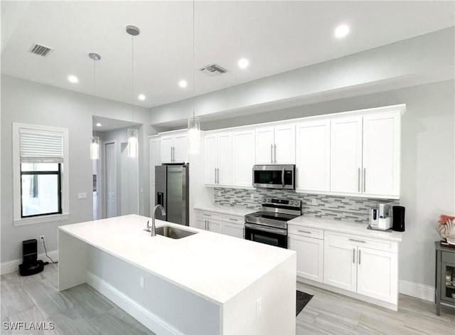 kitchen featuring tasteful backsplash, visible vents, an island with sink, stainless steel appliances, and a sink