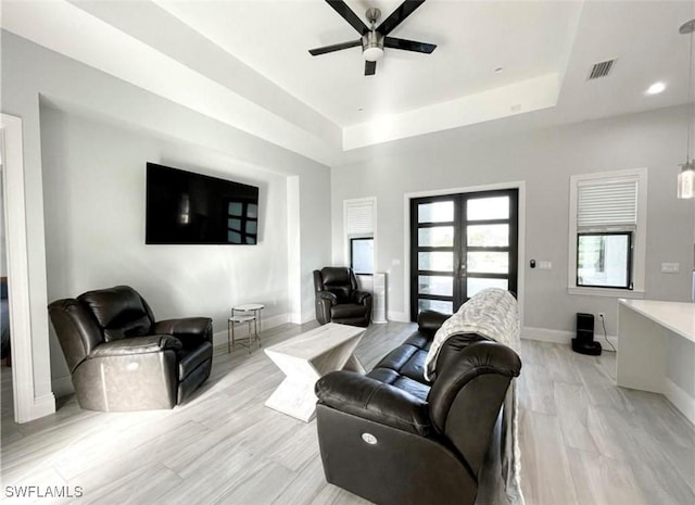 living area featuring visible vents, baseboards, a raised ceiling, and a ceiling fan