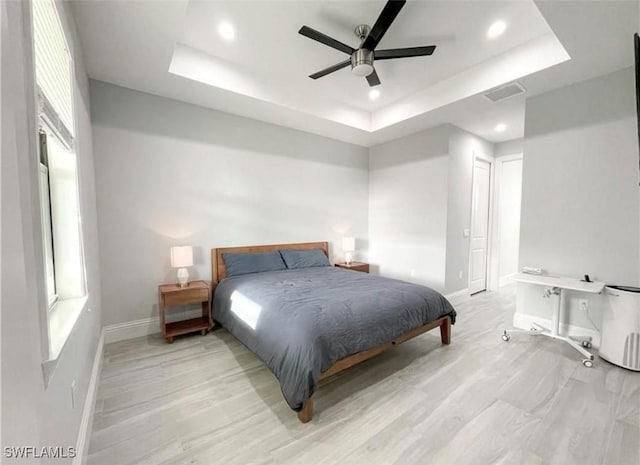 bedroom featuring multiple windows, baseboards, a raised ceiling, and light wood-style floors