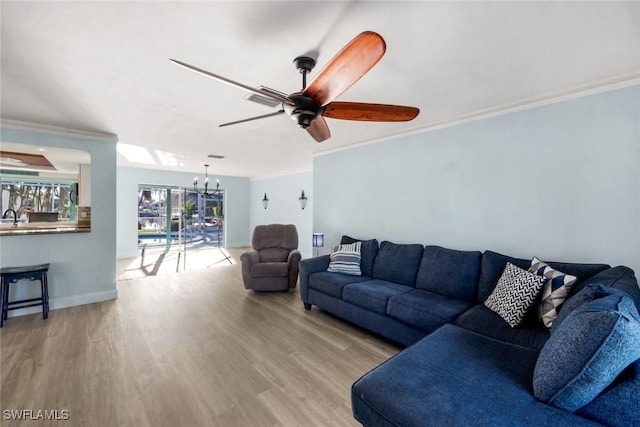 living room featuring baseboards, wood finished floors, ornamental molding, and ceiling fan with notable chandelier