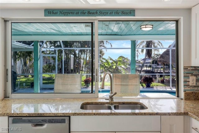 kitchen with a sink, light stone counters, stainless steel dishwasher, and white cabinetry