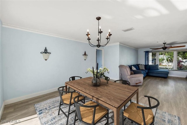 dining area with visible vents, light wood-style flooring, ceiling fan with notable chandelier, crown molding, and baseboards