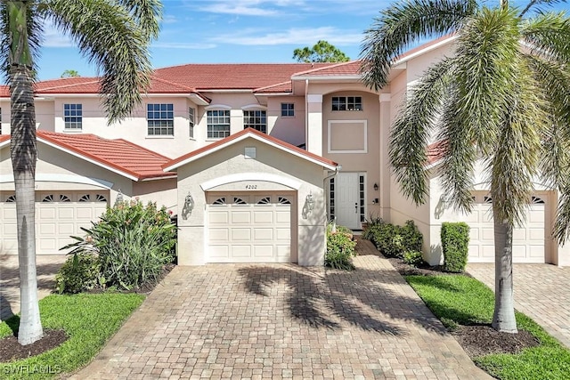 mediterranean / spanish-style home with a tile roof, decorative driveway, an attached garage, and stucco siding