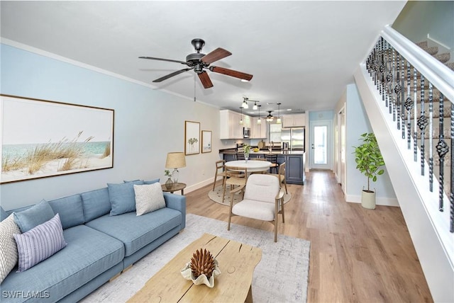 living room with crown molding, light wood-style floors, stairway, and a ceiling fan