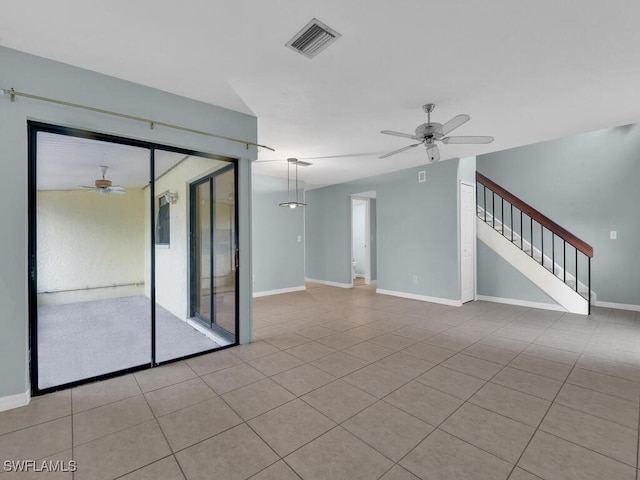 empty room featuring tile patterned floors, visible vents, baseboards, ceiling fan, and stairs