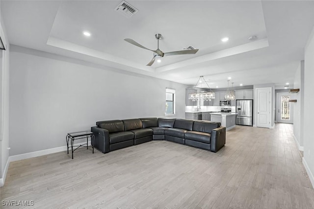 living room featuring visible vents, a raised ceiling, baseboards, and light wood finished floors