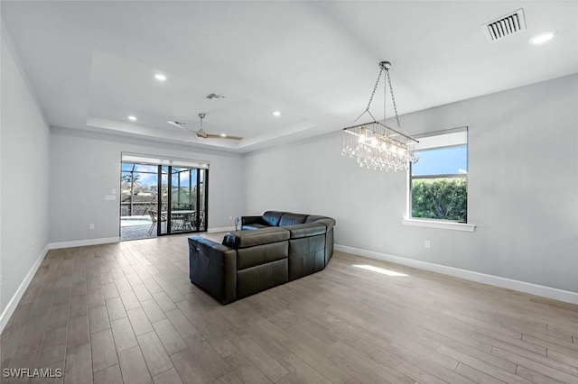 living area with visible vents, a healthy amount of sunlight, a tray ceiling, and wood finished floors