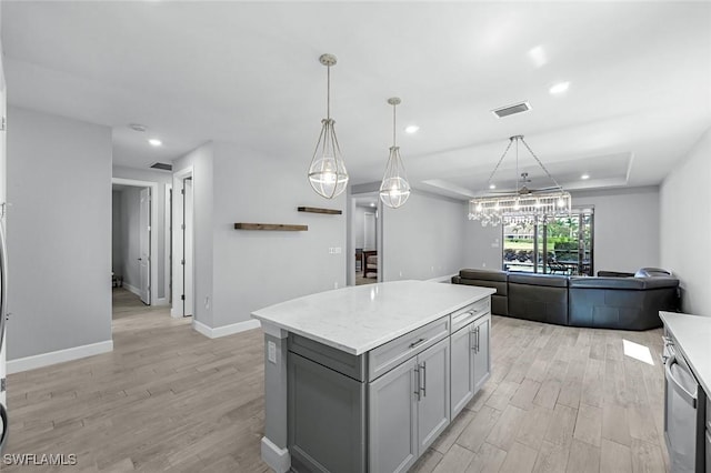 kitchen featuring visible vents, light wood-type flooring, gray cabinetry, a tray ceiling, and a kitchen island