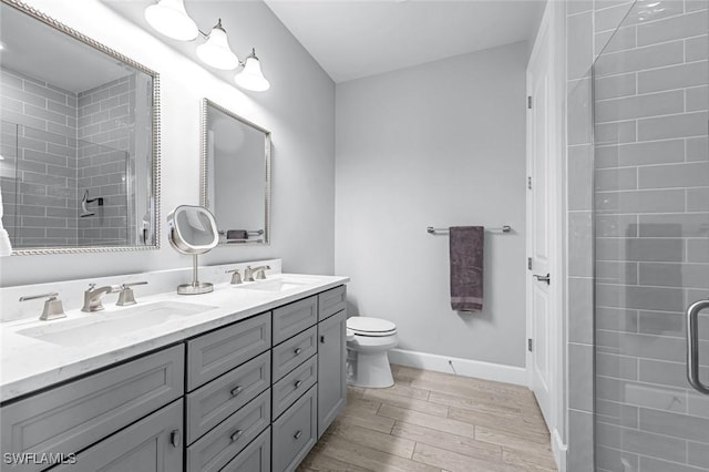 bathroom with a tile shower, double vanity, wood finished floors, and a sink