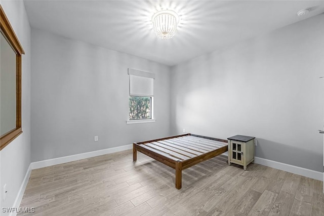 bedroom featuring light wood-style flooring, a notable chandelier, and baseboards