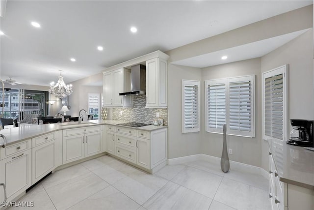 kitchen with tasteful backsplash, wall chimney range hood, a notable chandelier, black electric cooktop, and a sink