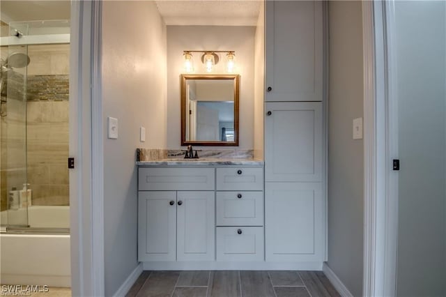 bathroom with vanity, baseboards, and bath / shower combo with glass door