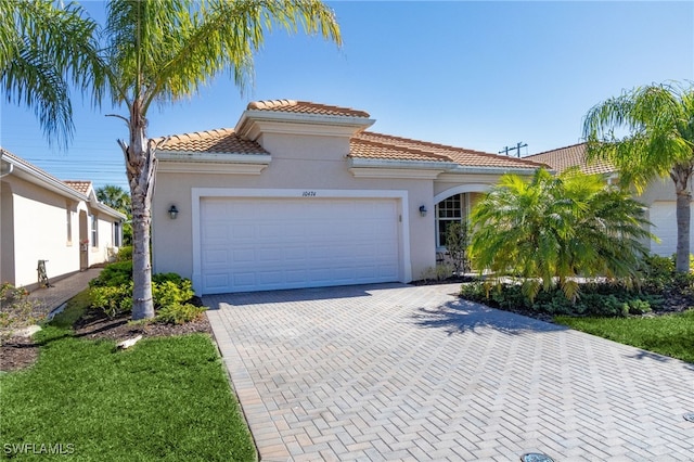 mediterranean / spanish-style home featuring stucco siding, a tile roof, decorative driveway, and a garage