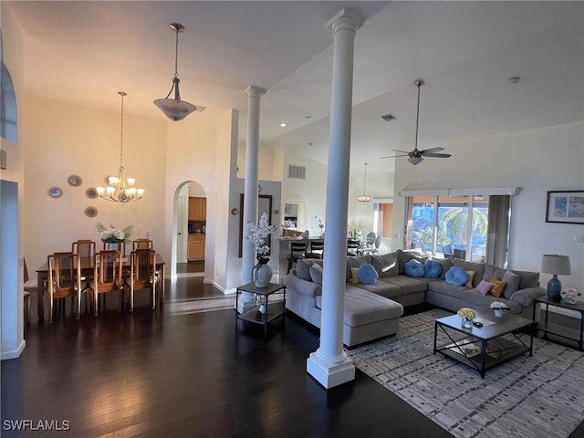 living room with visible vents, ornate columns, high vaulted ceiling, dark wood-style flooring, and ceiling fan with notable chandelier