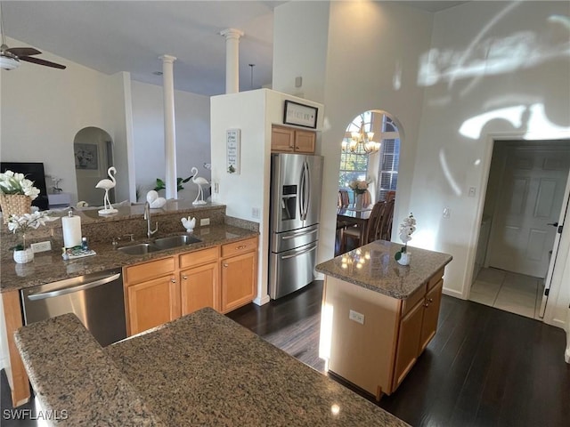 kitchen featuring a sink, dark stone countertops, ceiling fan with notable chandelier, stainless steel appliances, and dark wood-style flooring