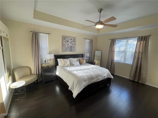 bedroom featuring dark wood finished floors, a tray ceiling, baseboards, and ceiling fan