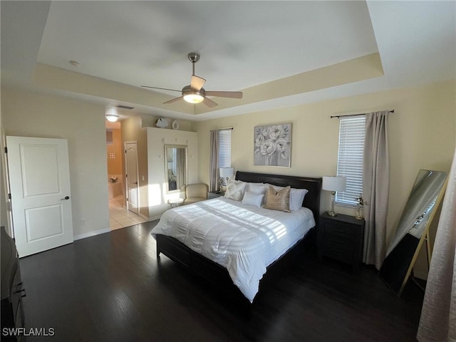 bedroom with a tray ceiling, wood finished floors, baseboards, and ensuite bathroom