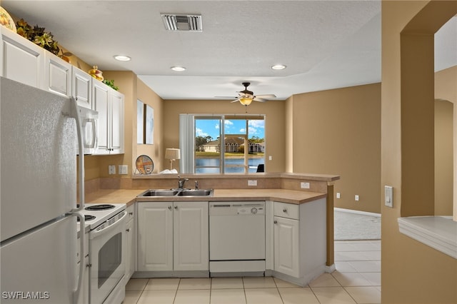 kitchen featuring visible vents, a peninsula, white appliances, a ceiling fan, and a sink