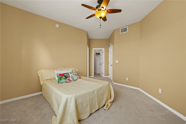 bedroom with visible vents, baseboards, ceiling fan, a walk in closet, and light colored carpet