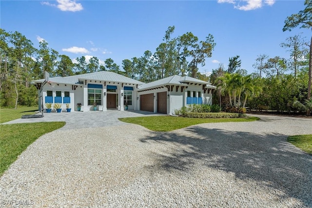 view of front of house with a front yard, stucco siding, metal roof, driveway, and an attached garage