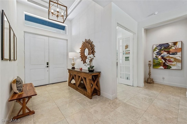 entryway with a high ceiling, a notable chandelier, baseboards, and light tile patterned floors