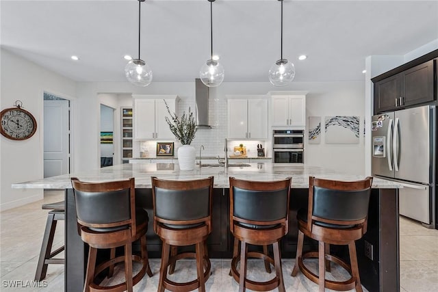 kitchen with white cabinetry, appliances with stainless steel finishes, wall chimney range hood, decorative backsplash, and light stone countertops