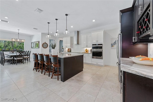 kitchen featuring tasteful backsplash, double oven, light tile patterned floors, white cabinets, and wall chimney exhaust hood