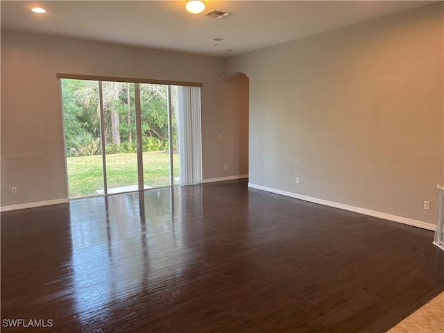 empty room featuring visible vents, baseboards, dark wood finished floors, recessed lighting, and arched walkways